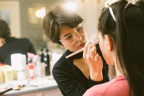 Woman wearing glasses doing someone's make up 