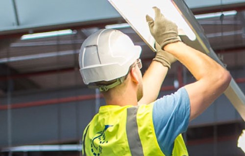 Electrician wearing hard hat changing warehouse lightbulb