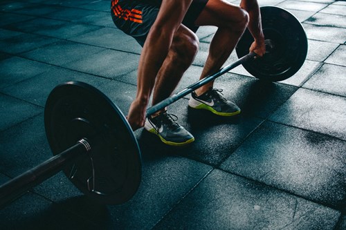 person bent down to lift a bar of weights