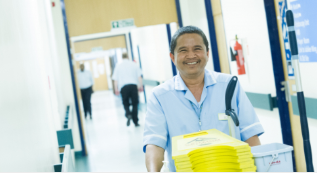 Healthcare cleaner pushing their trolly smiling 