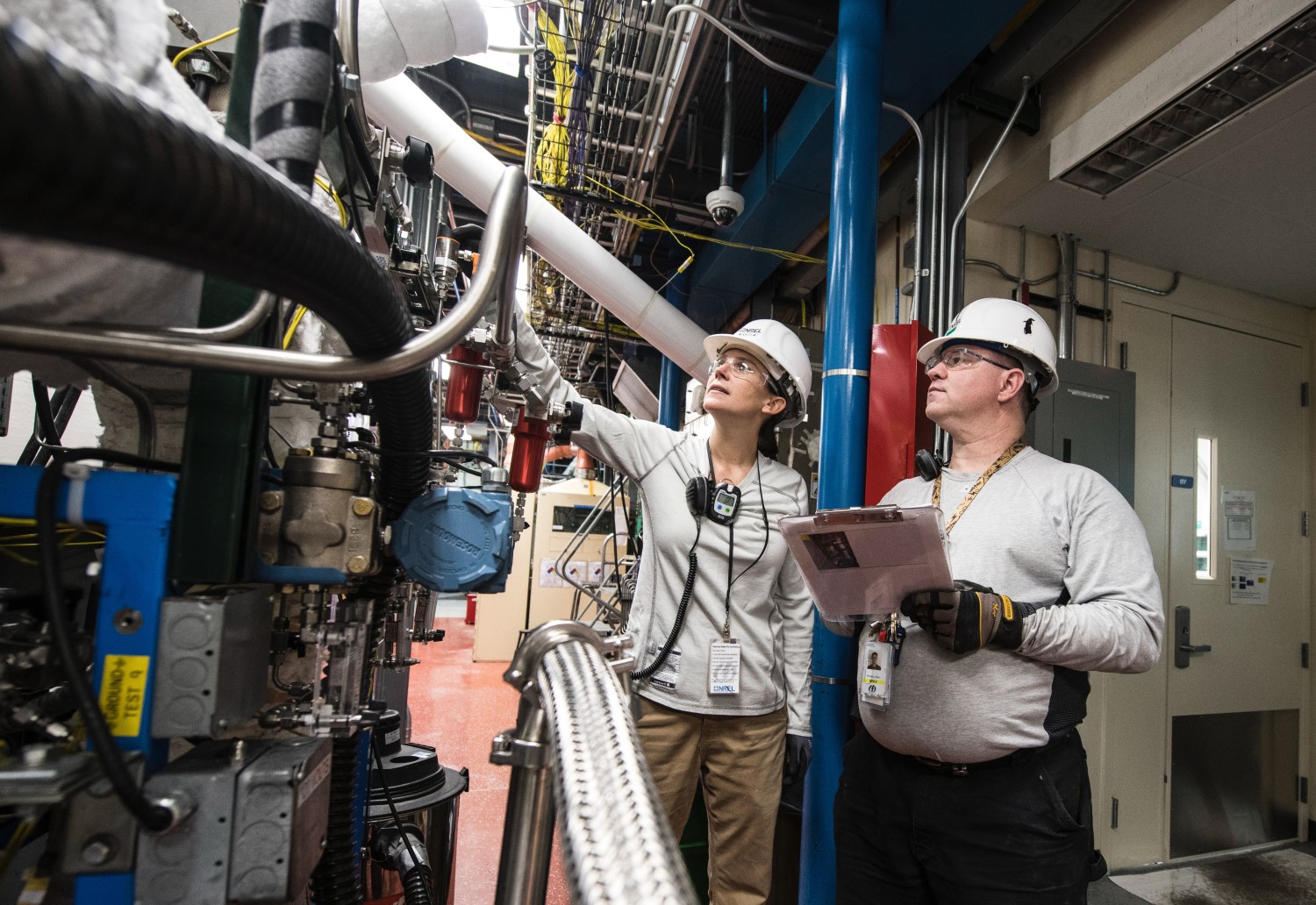 man and woman wearing hard hats inspecting machinery 