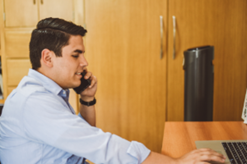 Man wearing a shirt on the phone working on a laptop