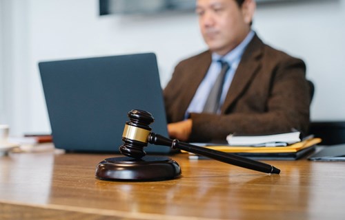Man wearing brown jacket working at a laptop with a gavel on desk 