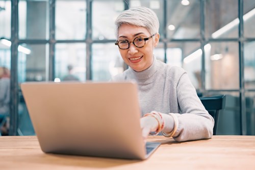 A woman over 50 wearing glasses working on a laptop