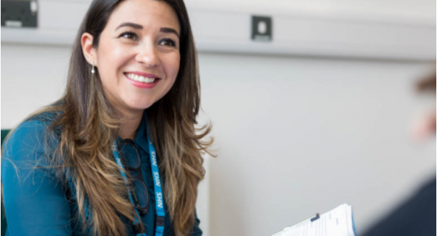 Woman smiling with long brown hair wearing a blue NHS lanyard