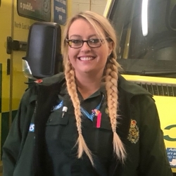 NHS paramedic with blonde hair in plaits smiling at the camera 