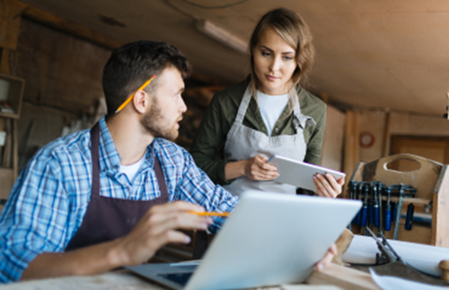 Man with pencil behind his ear talking to young woman wearing workshop overalls