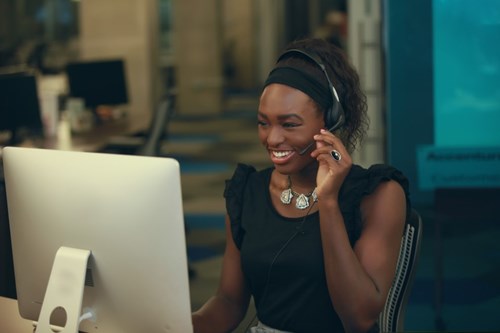 Woman smiling talking with a headset sat at a computer 