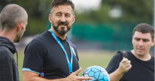 Man in black sportswear holding a football wearing a blue lanyard 