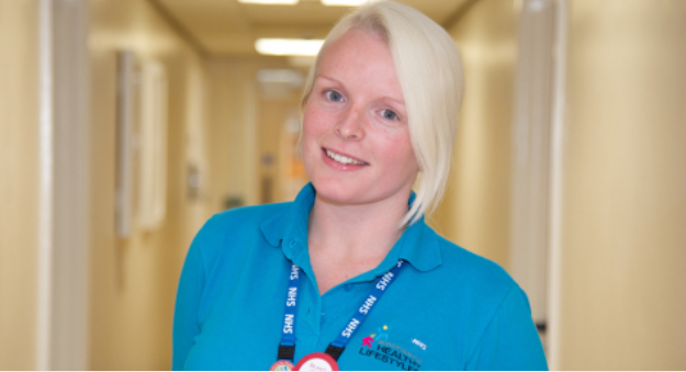 Woman with blonde hair wearing a blue NHS lanyard smiling at the camera 