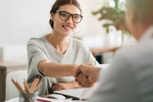 Woman wearing glasses and hoop earings smiling shaking hands with someone across the desk 