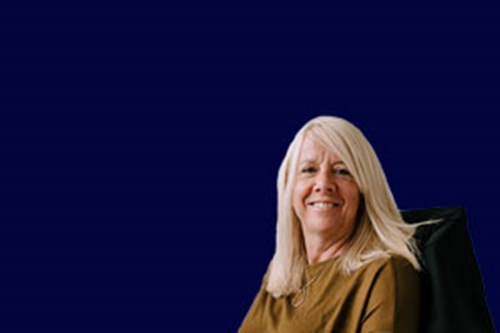 Over 50s woman with blonde hair sat at an office desk smiling 